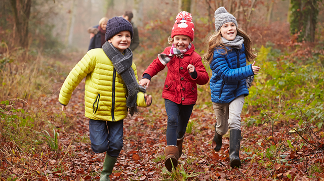 Three smiley children wrapped up warm and running through a wet woodland